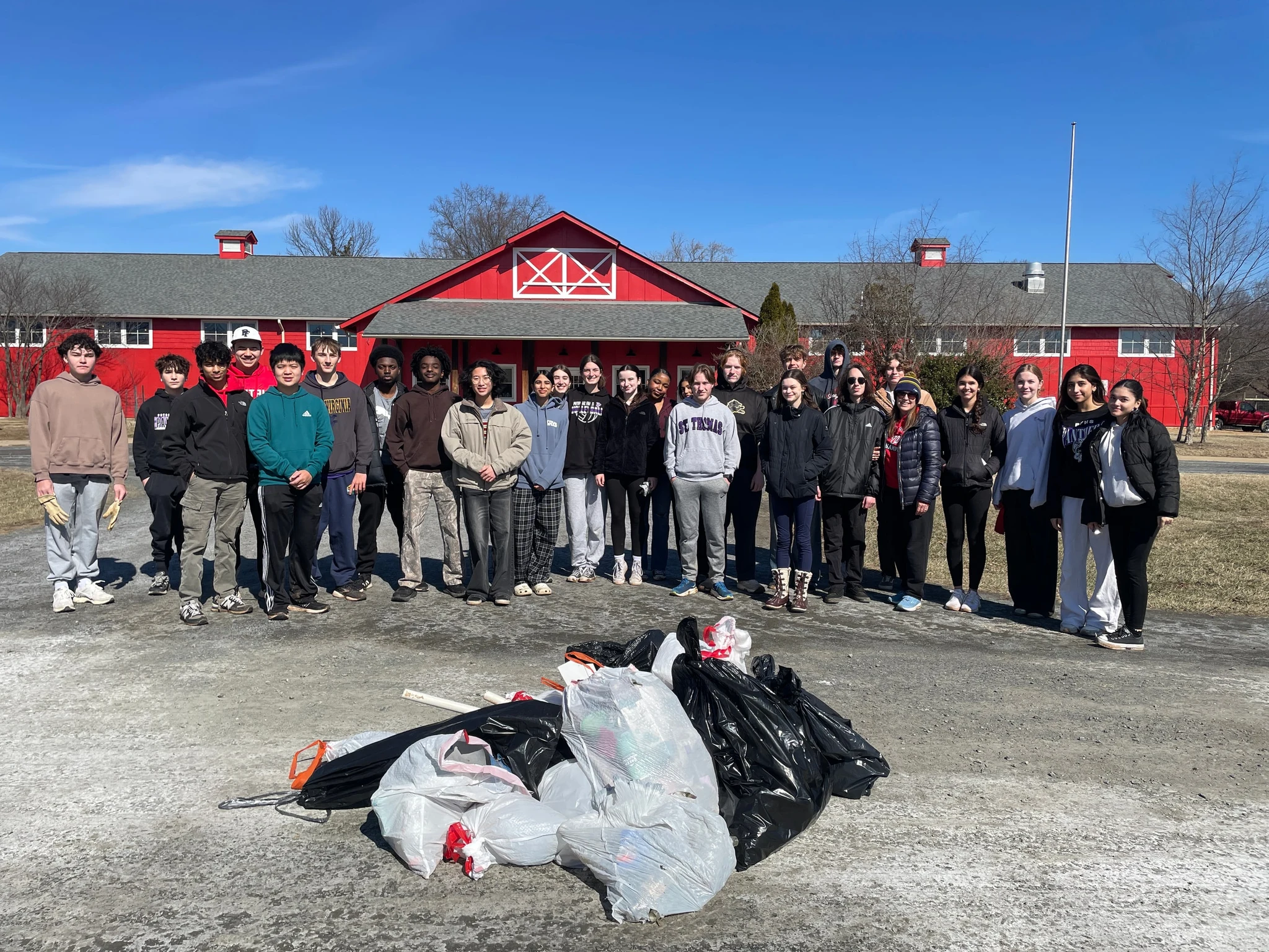 Volunteers standing in front of a red barn, with bags of collected trash piled in the foreground