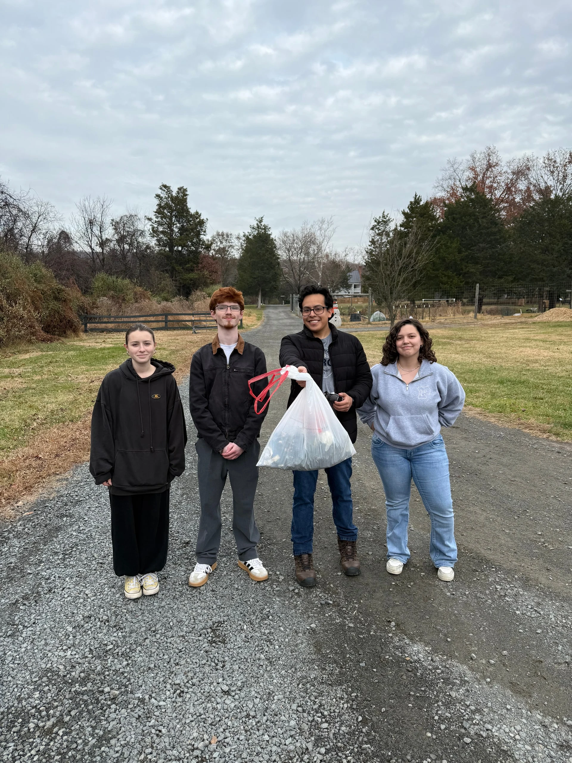 Four volunteers standing on a gravel lane, one holding a bag of collected trash